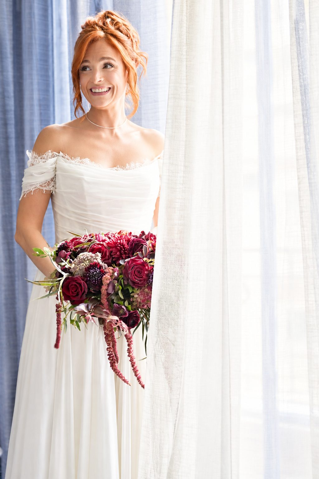 Bride smiling beside a window, holding her bouquet