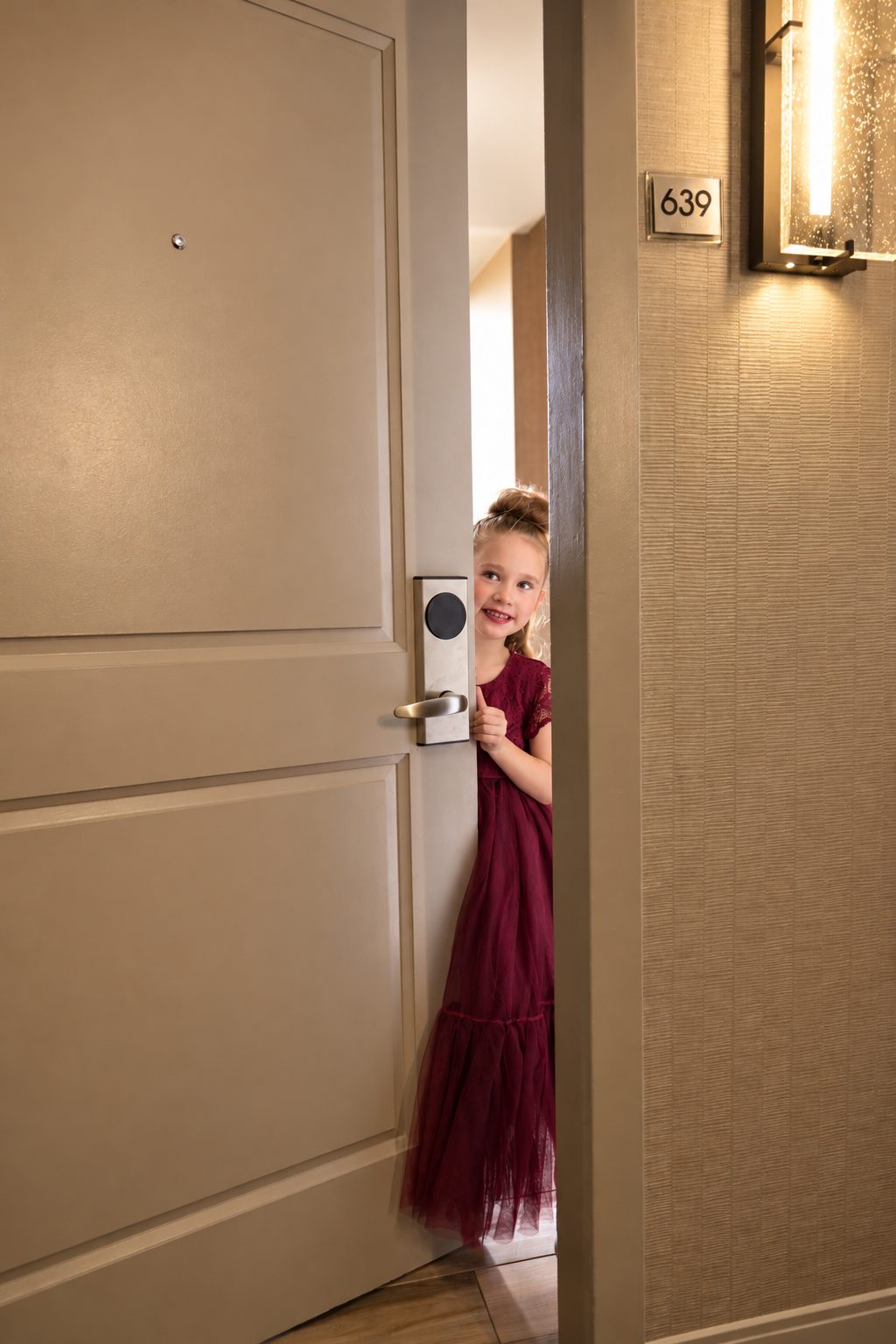 Flower girl peeking through a hotel room door