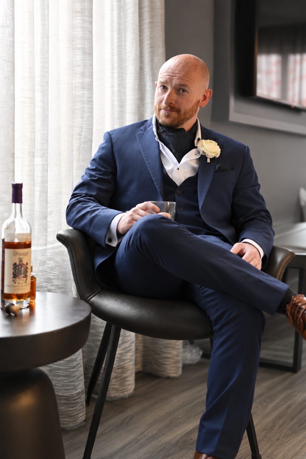 Groom seated in a chair with a glass of whiskey, getting ready