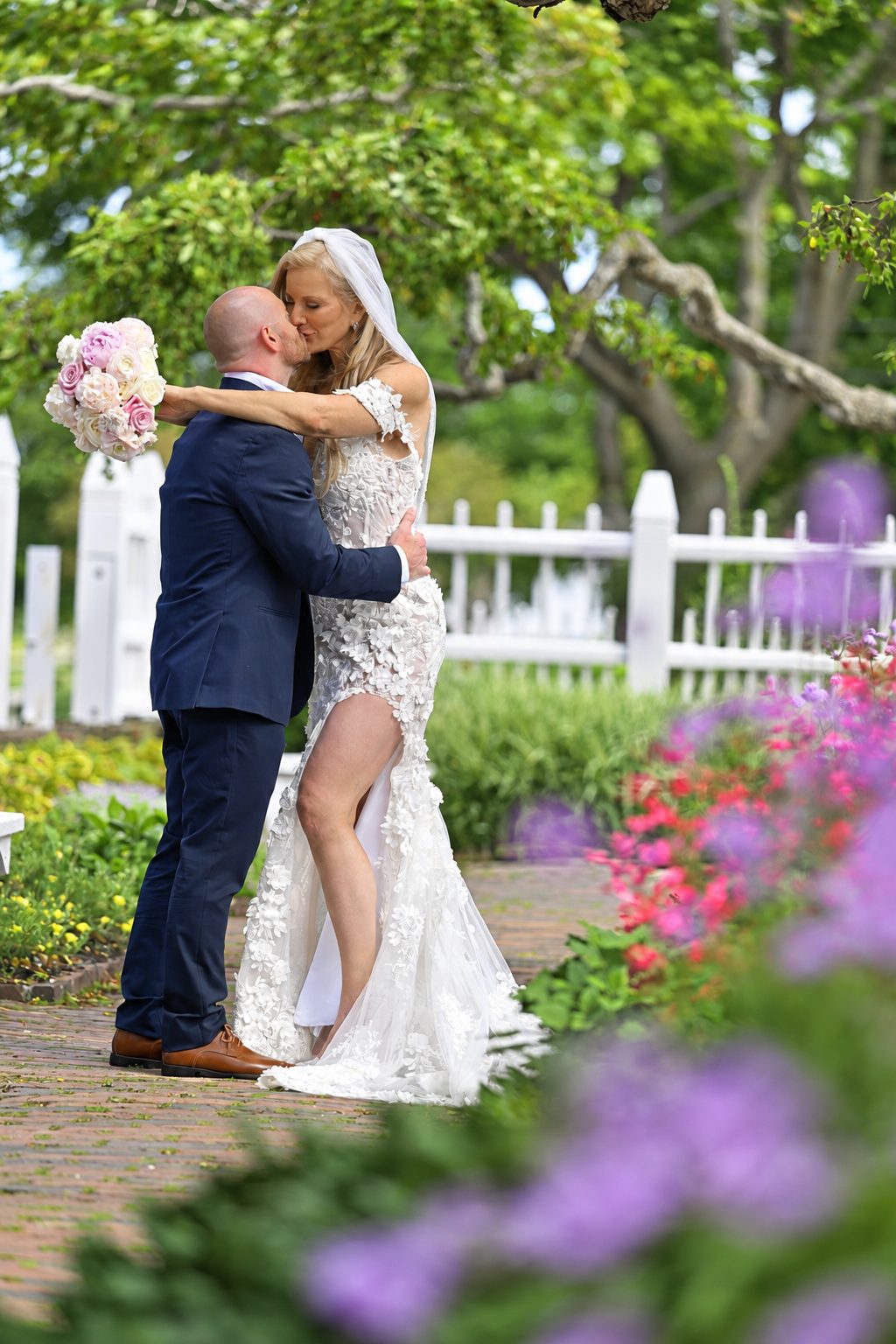 Bride and groom kiss in a garden by a white picket fence