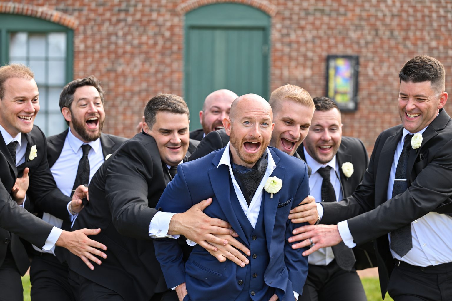 Groomsmen laughing and grabbing the groom playfully